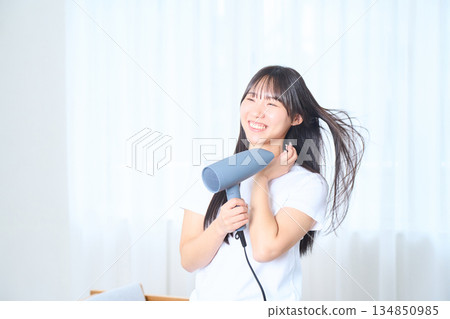 A Japanese woman using a hair dryer in a bright living room 134850985