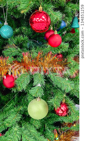 Close-up of a decorated Christmas tree with colorful shiny balls, sparkling tinsel and ornaments Close-up of a decorated Christmas tree with colorful shiny balls, sparkling tinsel and ornaments 134851259