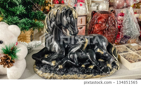 Black and gold horse with foal figurine on a store shelf surrounded by festive Christmas decorations Black and gold horse with foal figurine on a store shelf surrounded by festive Christmas decorations 134851565