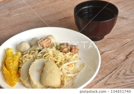 dry boiled Chinese yellow egg noodles dory fish and fishball with bean sprout topping crispy dumpling on plate and soup in cup 134851740