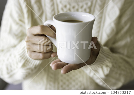 一位身穿針織毛衣的人雙手捧著一杯熱咖啡(特寫鏡頭) 一位身穿針織毛衣的人雙手捧著一杯熱咖啡(特寫鏡頭) 134853217