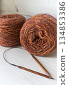 Warm brown yarn with wooden knitting needles on white background. Knitting needles and balls of orange yarn. Soft merino yarn ball and needles. Knitting hobby. Knitwear concept. Knitted fashion. 134853386