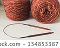 Warm brown yarn with wooden knitting needles on white background. Knitting needles and balls of orange yarn. Soft merino yarn ball and needles. Knitting hobby. Knitwear concept. Knitted fashion. 134853387