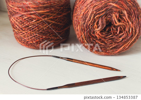 Warm brown yarn with wooden knitting needles on white background. Knitting needles and balls of orange yarn. Soft merino yarn ball and needles. Knitting hobby. Knitwear concept. Knitted fashion. 134853387