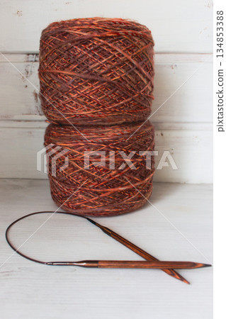 Warm brown yarn with wooden knitting needles on white background. Knitting needles and balls of orange yarn. Soft merino yarn ball and needles. Knitting hobby. Knitwear concept. Knitted fashion. 134853388