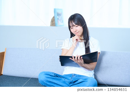 A Japanese woman opening a notebook and thinking Image of ideas, future plans, and studying 134854631
