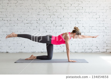 Slim Caucasian woman practice bird dog drill exercise standing on all fours with one leg and arm up in loft fitness studio. Slim Caucasian woman practice bird dog drill exercise standing on all fours with one leg and arm up in loft fitness studio. 134854658