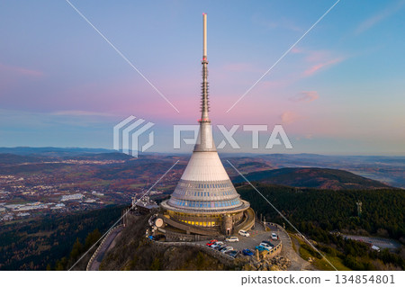 Jested mountain hotel during sunset. The drone view captures the hotel and surrounding landscape in Liberec. The sky glows with evening colors. 134854801