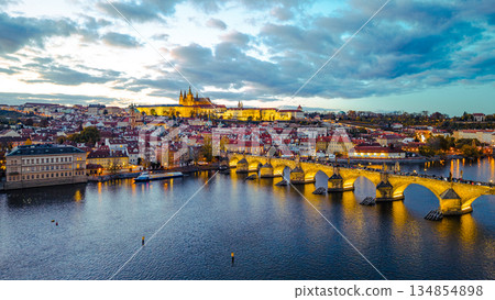 An aerial view shows illuminated Prague Castle and Charles Bridge at night. The Vltava River reflects city lights, creating a vibrant scene in Prague, Czechia. An aerial view shows illuminated Prague Castle and Charles Bridge at night. The Vltava River reflects city lights, creating a vibrant scene in Prague, Czechia. 134854898