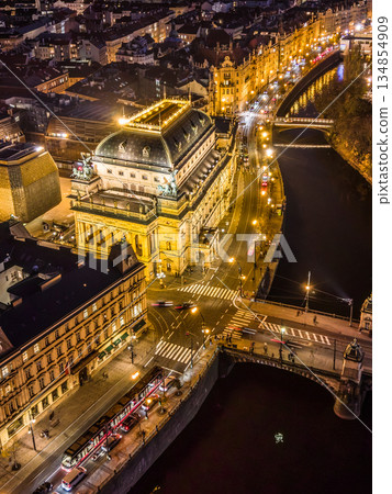 Aerial view shows the National Theatre in Prague illuminated at night. The Smetana embankment and Rasin are seen with lights reflecting on the water. Aerial view shows the National Theatre in Prague illuminated at night. The Smetana embankment and Rasin are seen with lights reflecting on the water. 134854909