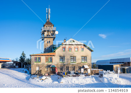 The photograph shows the Tanvaldsky Spicak Lookout Tower covered in snow during winter. People visit this resort in the Jizera Mountains for scenic views and outdoor activities. The photograph shows the Tanvaldsky Spicak Lookout Tower covered in snow during winter. People visit this resort in the Jizera Mountains for scenic views and outdoor activities. 134854919