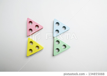Minimalist pastel colored wooden triangle shapes with three drilled holes arranged on a white background. A simple still life suitable for childhood, learning, and creative play 134855088