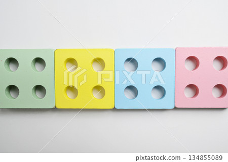Colorful wooden square blocks with four holes, arranged in a row on a white background. Concept of early childhood education, toys, learning, and playing Colorful wooden square blocks with four holes, arranged in a row on a white background. Concept of early childhood education, toys, learning, and playing 134855089