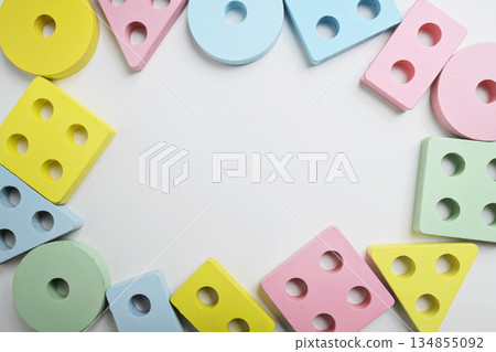 Top view of assorted wooden shape sorter toys in pastel colors, arranged in a circle on a white surface. The shapes include squares, circles, and triangles 134855092
