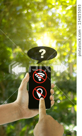 Human hand holding a smartphone displaying icons for no wifi connection and no location service. A question mark speech bubble is above the phone, indicating confusion or a problem. Concept of lost 134855093