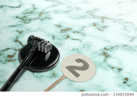 Black gavel resting on its stand next to a paddle with the number two on a light marble background. Ideal for concepts of law, auctions, or legal processes Black gavel resting on its stand next to a paddle with the number two on a light marble background. Ideal for concepts of law, auctions, or legal processes 134855099