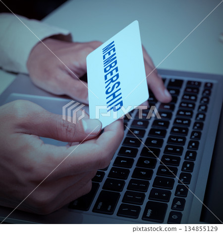 Business hand holding a membership card in their hand, over a laptop keyboard. The scene suggests online enrollment, digital access, or management of a membership account 134855129