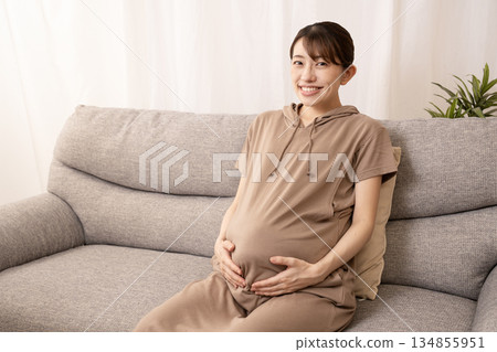An eight-month pregnant woman sitting on a sofa and rubbing her stomach 134855951