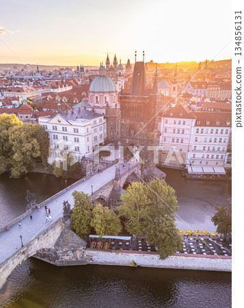 An aerial view of the Old Town Bridge Tower at Charles Bridge in Prague, capturing the beauty of the Vltava River and the vibrant city skyline during sunset. 134856131