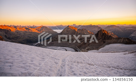 The sun rises over Pers Glacier, illuminating the Bernina Range's rugged peaks. The serene landscape showcases the breathtaking beauty of the Swiss Alps at dawn. 134856150