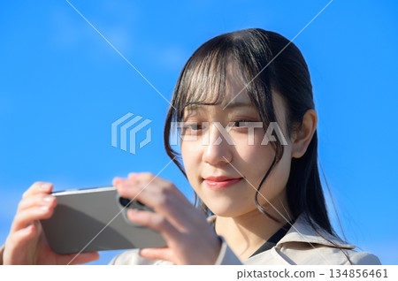 A woman using a smartphone with a blue sky in the background A woman using a smartphone with a blue sky in the background 134856461