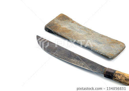 A well-used bolo knife and a whetstone are placed on a plain white background. Both items show signs of age and wear. 134856831