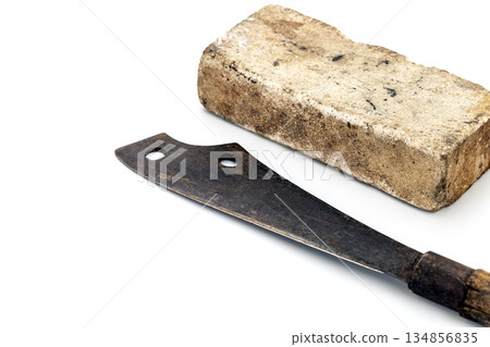 A big thick whetstone rests near a rusty machete on a white surface. 134856835