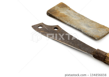 On white, a vintage rusty cleaver with a wooden handle lies next to a sharpening stone. Both show signs of age. On white, a vintage rusty cleaver with a wooden handle lies next to a sharpening stone. Both show signs of age. 134856838