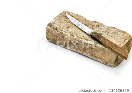 A slightly rusted metal knife with a wooden handle laying on a big thick whetstone in a studio shot. 134856839