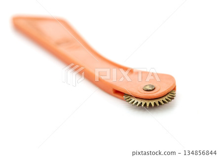 A vintage tracing wheel, used for marking patterns onto fabric, is set against a clean white backdrop. 134856844