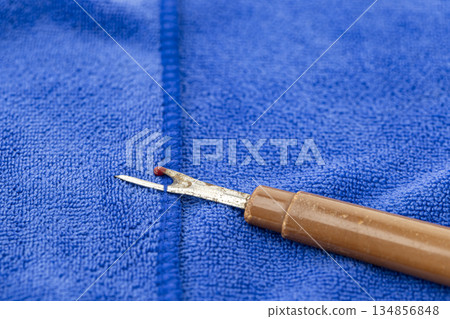 Close-up of a seam ripper with a brown handle and a small red ball, lying on a vibrant blue fabric. 134856848