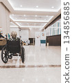 Rear view of a senior woman sitting in a wheelchair inside a modern hospital lobby with bright lighting and spacious interior. Healthcare concept representing elderly care, patient support, accessibil 134856885