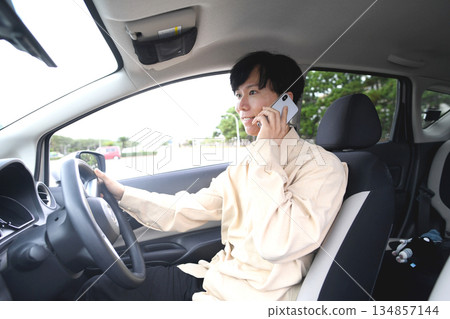 A young man driving a car while talking on his smartphone 134857144