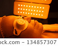 Client receiving a skincare treatment under orange light therapy 134857307