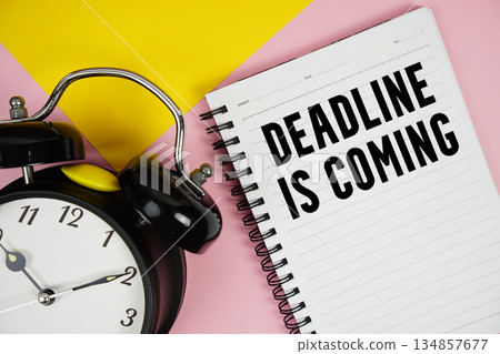 Deadline is Coming text written on notepad with alarm clock on pink background Deadline is Coming text written on notepad with alarm clock on pink background 134857677