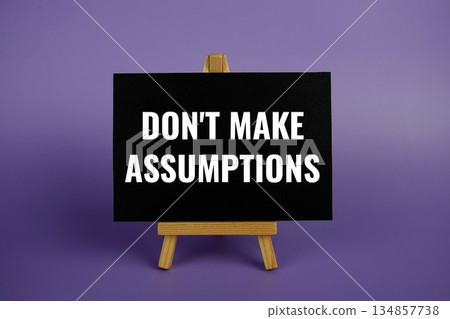 Don't Make Assumptions text written on paper card with wooden easel on purple background 134857738