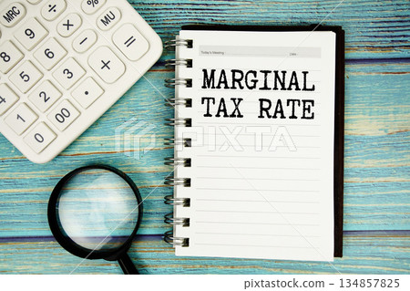Marginal Tax Rate text on notepad with magnifying glass and calculator on wooden background Marginal Tax Rate text on notepad with magnifying glass and calculator on wooden background 134857825
