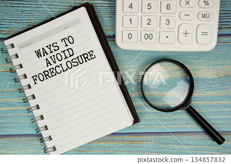 Ways To Avoid Foreclosure text on notepad with magnifying glass and calculator on wooden background 134857832