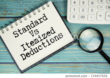 Standard Vs Itemized Deductions text on notepad with magnifying glass and calculator on wooden background 134857836