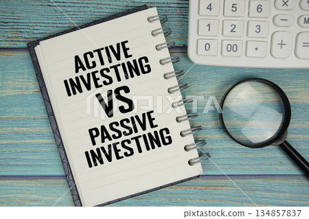 Active vs Passive Investing text on notepad with magnifying glass and calculator on wooden background 134857837