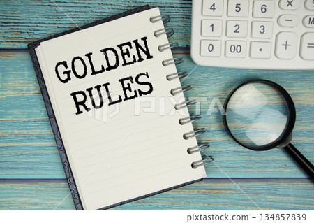 Golden Rules text on notepad with magnifying glass and calculator on wooden background 134857839