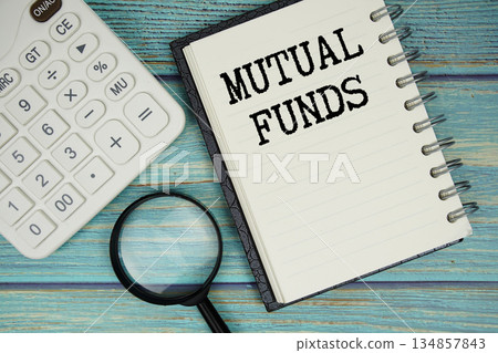 Mutual Funds text on notepad with magnifying glass and calculator on wooden background Mutual Funds text on notepad with magnifying glass and calculator on wooden background 134857843