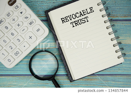 Revocable Trust text on notepad with magnifying glass and calculator on wooden background 134857844