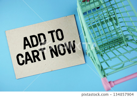 Add to Cart Now text on paper card with trolley shopping cart on blue background Add to Cart Now text on paper card with trolley shopping cart on blue background 134857904