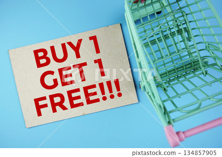 Buy 1, Get 1 Free text on paper card with trolley shopping cart on blue background Buy 1, Get 1 Free text on paper card with trolley shopping cart on blue background 134857905