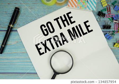 Go The Extra Mile text written on notepad with magnifying glass flat lay on wooden background Go The Extra Mile text written on notepad with magnifying glass flat lay on wooden background 134857954