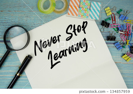 Never Stop Learning text on a paper surrounded by office supplies and magnifying glass on a blue wooden surface Never Stop Learning text on a paper surrounded by office supplies and magnifying glass on a blue wooden surface 134857959