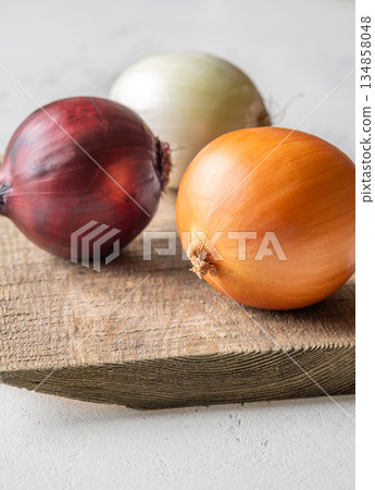 Three whole onions on rustic board showing red, yellow, and white varieties 134858048