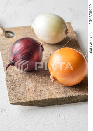 Three whole onions on rustic board showing red, yellow, and white varieties Three whole onions on rustic board showing red, yellow, and white varieties 134858049