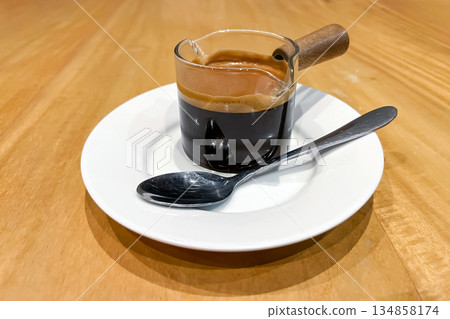 glass espresso measuring cup with a wooden handle that sits on a white saucer 134858174